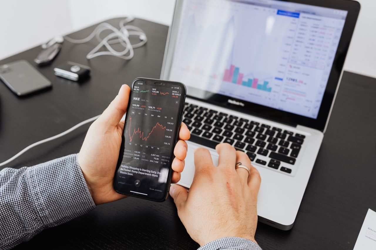 heros-img Person analyzes stock data with a smartphone and laptop, indoors.